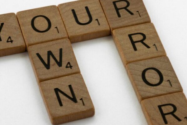 Wooden Scrabble tiles forming the motivational phrase 'Own Your Error' on a white background.